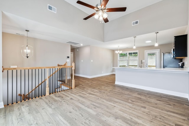 empty room featuring ceiling fan with notable chandelier, high vaulted ceiling, sink, and hardwood / wood-style floors