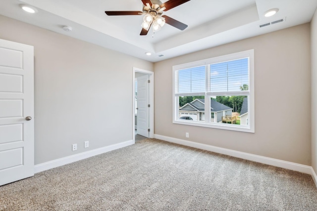 unfurnished room with a raised ceiling, carpet, and ceiling fan