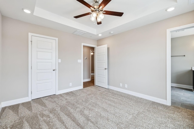 unfurnished bedroom featuring a tray ceiling, ceiling fan, and carpet flooring