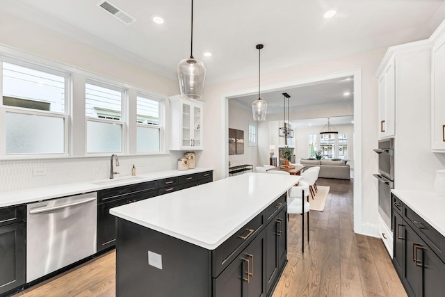 kitchen with sink, white cabinetry, stainless steel appliances, a kitchen island, and light wood-type flooring