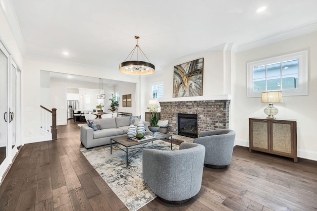 living room featuring hardwood / wood-style floors, ornamental molding, a chandelier, and a brick fireplace