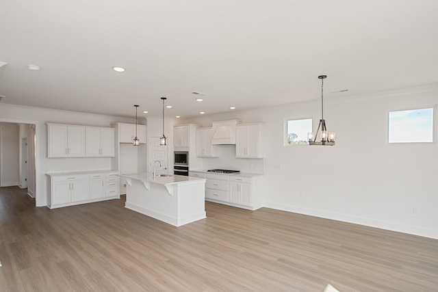 kitchen featuring gas stovetop, decorative light fixtures, an island with sink, custom range hood, and white cabinets