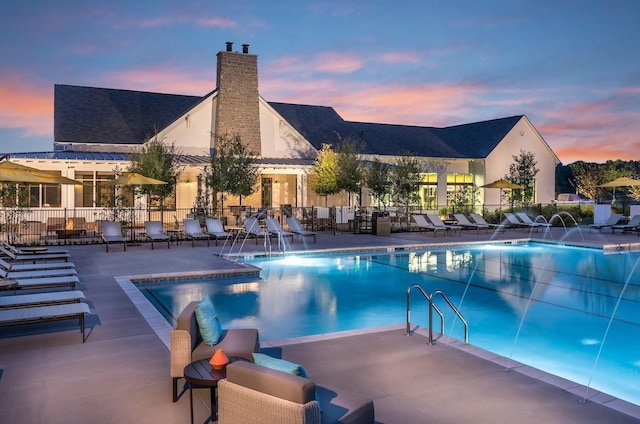 pool at dusk with pool water feature and a patio area