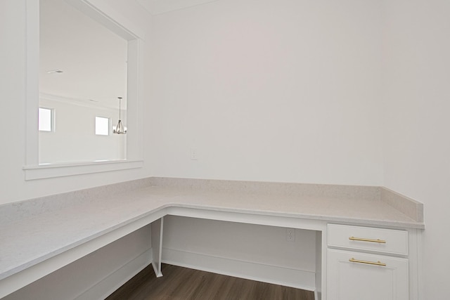 unfurnished office with dark wood-type flooring, built in desk, and a chandelier