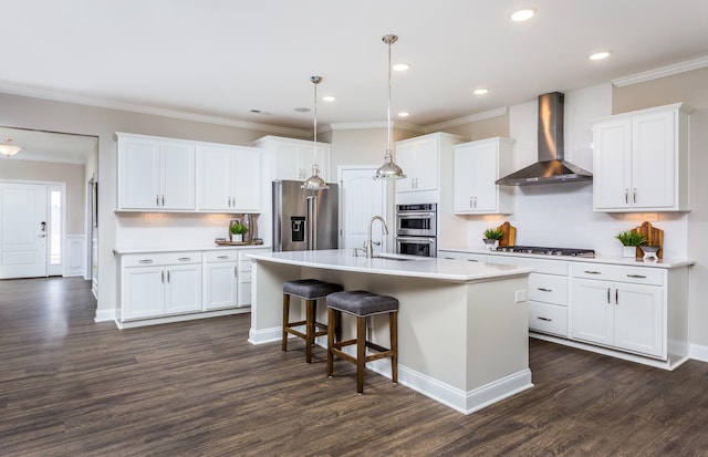 kitchen featuring white cabinetry, stainless steel appliances, a center island with sink, and wall chimney range hood