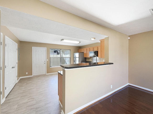 kitchen featuring stainless steel refrigerator with ice dispenser, kitchen peninsula, and sink