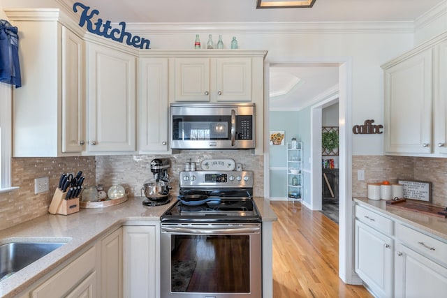 kitchen with appliances with stainless steel finishes, tasteful backsplash, ornamental molding, light stone counters, and light hardwood / wood-style floors