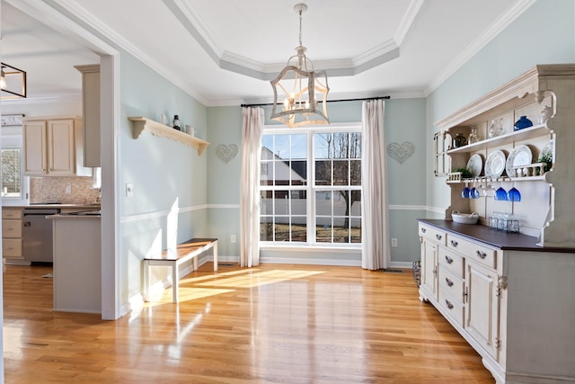 unfurnished dining area with a tray ceiling, ornamental molding, a chandelier, and light wood-type flooring