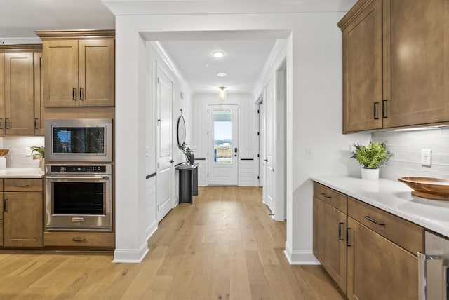 kitchen featuring built in microwave, oven, light hardwood / wood-style floors, and backsplash