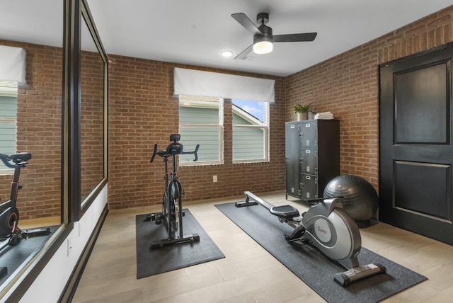 workout area featuring ceiling fan, brick wall, and light wood-type flooring