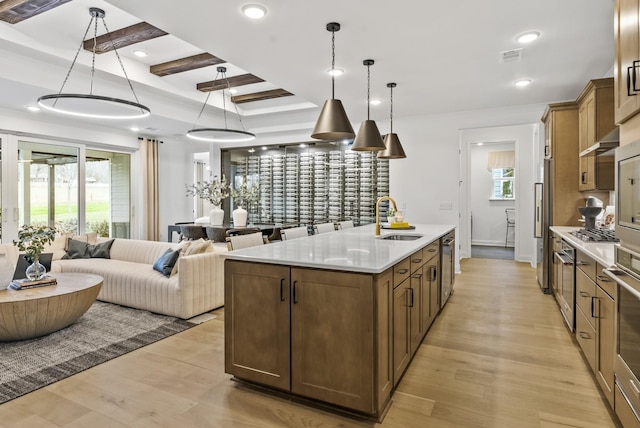 kitchen with sink, light hardwood / wood-style flooring, a kitchen island with sink, beam ceiling, and decorative light fixtures