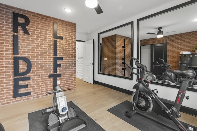 exercise room featuring ceiling fan, brick wall, and light hardwood / wood-style floors