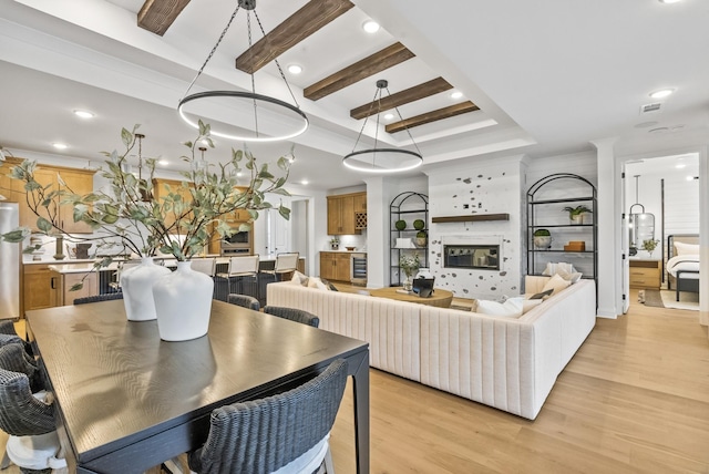 living room featuring beamed ceiling, a fireplace, a raised ceiling, and light wood-type flooring