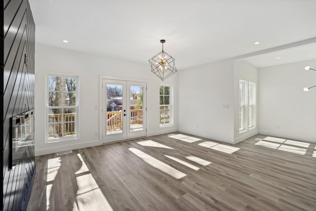 unfurnished living room featuring plenty of natural light, hardwood / wood-style floors, a notable chandelier, and french doors