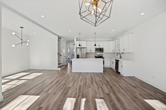 kitchen with white cabinetry, stainless steel appliances, a center island, decorative light fixtures, and light wood-type flooring