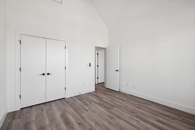 unfurnished bedroom featuring light wood-type flooring, high vaulted ceiling, and a closet