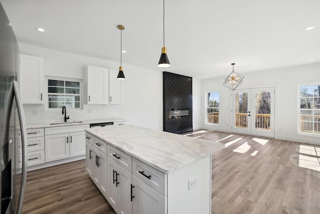 kitchen with sink, stainless steel fridge, white cabinetry, a kitchen island, and decorative light fixtures