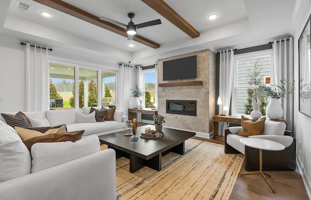 living room featuring a brick fireplace, a tray ceiling, beamed ceiling, ceiling fan, and light hardwood / wood-style floors