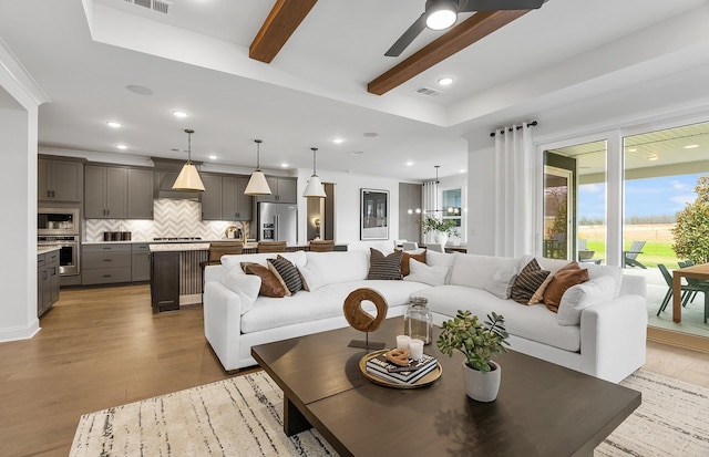 living room featuring beamed ceiling, ceiling fan, and light wood-type flooring