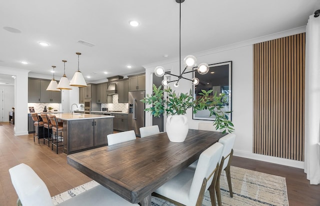 dining area with dark wood-type flooring, crown molding, sink, and a notable chandelier