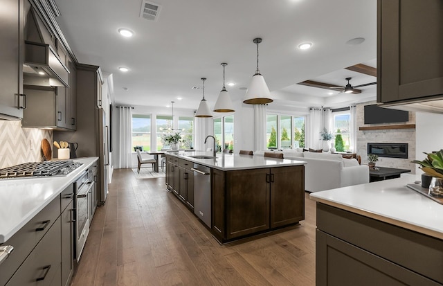 kitchen with pendant lighting, tasteful backsplash, sink, dark hardwood / wood-style flooring, and a center island with sink