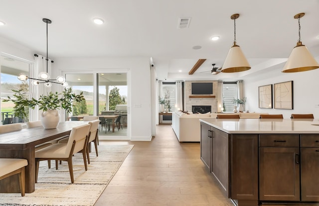 kitchen with dark brown cabinetry, decorative light fixtures, a large fireplace, and light wood-type flooring