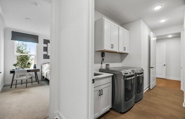 clothes washing area with cabinets, washing machine and dryer, and light hardwood / wood-style flooring