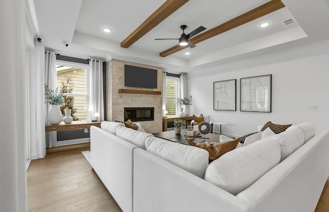 living room featuring ceiling fan, a brick fireplace, light wood-type flooring, and a tray ceiling