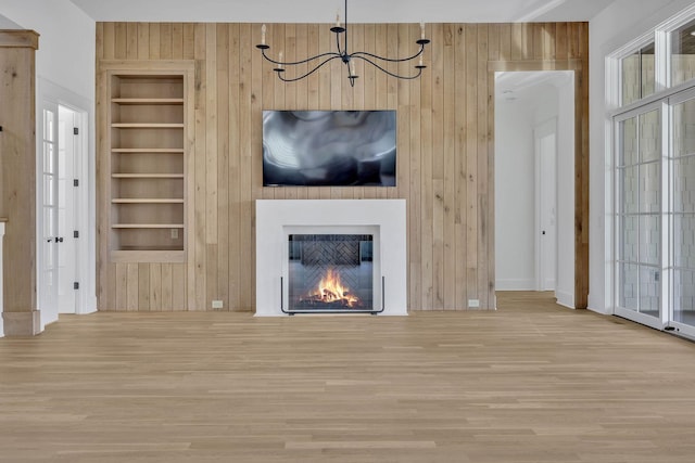 unfurnished living room with built in shelves, a notable chandelier, and light wood-type flooring