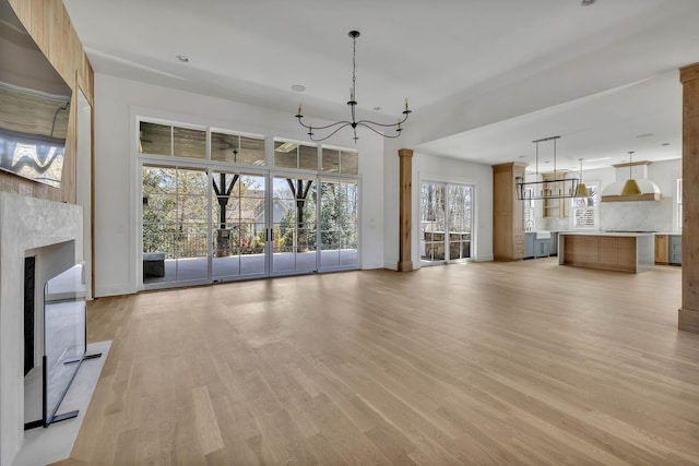 unfurnished living room featuring a fireplace, a chandelier, and light hardwood / wood-style flooring