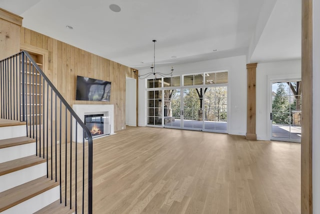 unfurnished living room with a notable chandelier, wooden walls, and light wood-type flooring