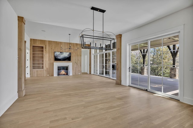 unfurnished living room featuring built in shelves, wooden walls, light hardwood / wood-style floors, and a chandelier