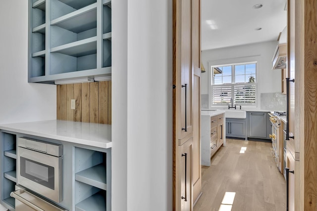 kitchen with sink, gray cabinetry, gas range, light hardwood / wood-style flooring, and stainless steel microwave