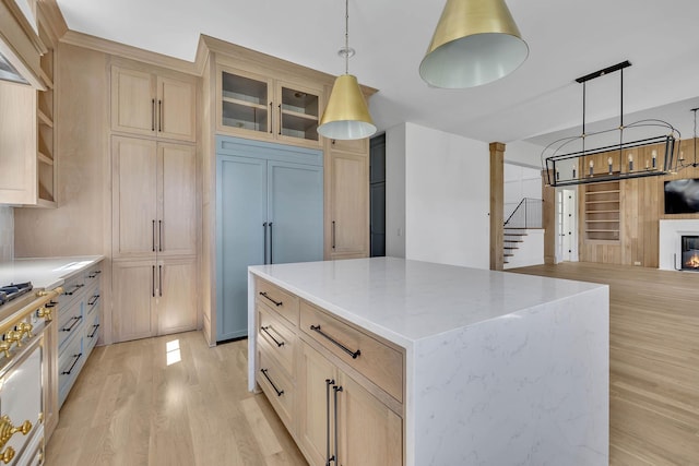 kitchen featuring ornate columns, light stone counters, decorative light fixtures, a center island, and light wood-type flooring