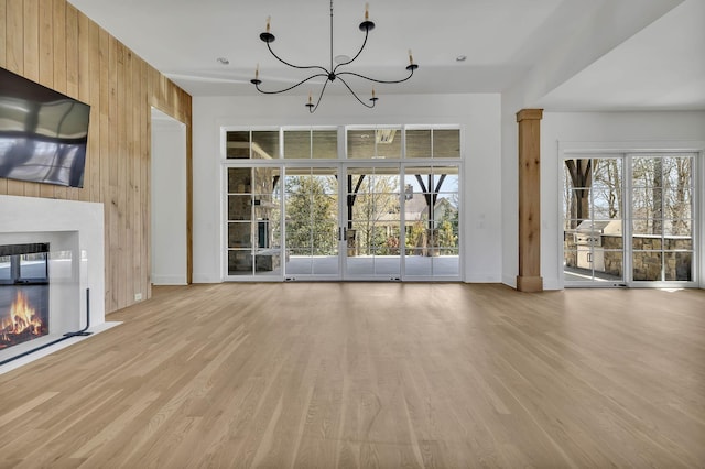 unfurnished living room with light hardwood / wood-style flooring, wooden walls, and an inviting chandelier