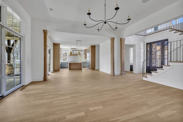 unfurnished living room featuring ornate columns, an inviting chandelier, and light wood-type flooring