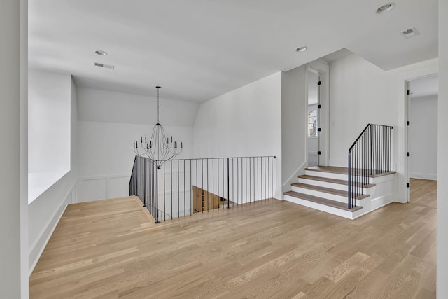 hallway with lofted ceiling, light hardwood / wood-style floors, and an inviting chandelier