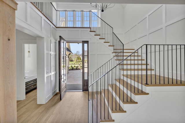 foyer entrance featuring a towering ceiling, a chandelier, and light wood-type flooring