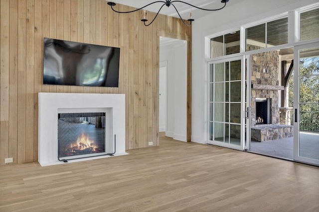 unfurnished living room featuring wooden walls, a fireplace, a chandelier, and light hardwood / wood-style flooring