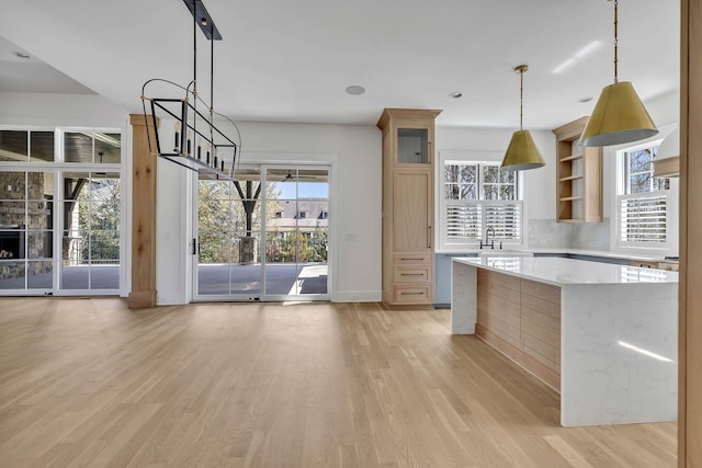 kitchen with sink, light stone counters, decorative light fixtures, stainless steel dishwasher, and light hardwood / wood-style floors