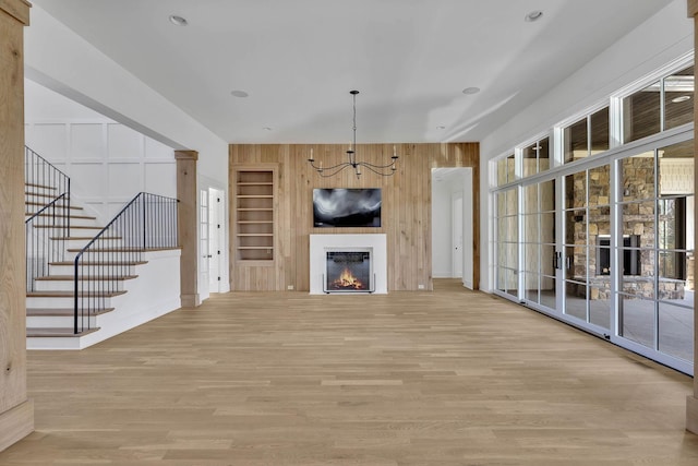 unfurnished living room featuring built in shelves, plenty of natural light, light hardwood / wood-style flooring, and wood walls