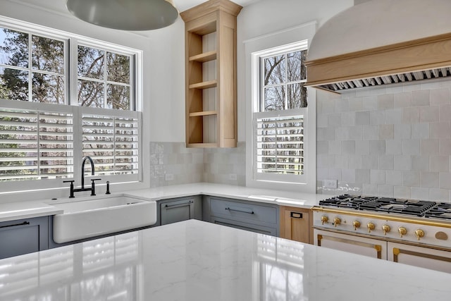 kitchen with sink, gray cabinets, premium range hood, light stone counters, and decorative backsplash