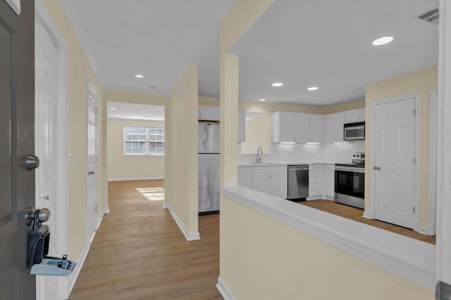 kitchen featuring sink, light hardwood / wood-style flooring, appliances with stainless steel finishes, tasteful backsplash, and white cabinets