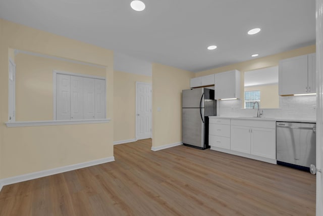 kitchen featuring sink, white cabinets, decorative backsplash, stainless steel appliances, and light wood-type flooring