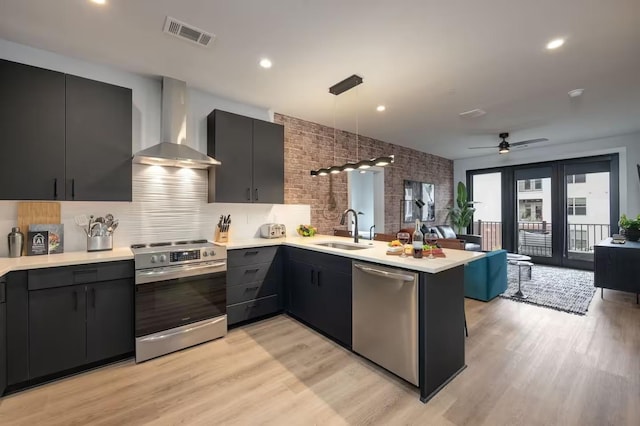 kitchen featuring appliances with stainless steel finishes, pendant lighting, sink, kitchen peninsula, and wall chimney exhaust hood