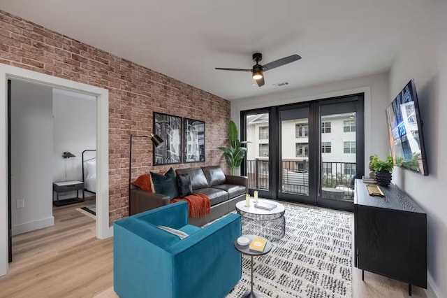 living room with ceiling fan, plenty of natural light, brick wall, and light wood-type flooring