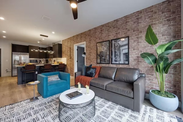 living room with light wood-type flooring, ceiling fan, and brick wall