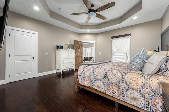 bedroom featuring a textured ceiling, dark wood-type flooring, a raised ceiling, and ceiling fan