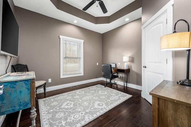 office area with dark wood-type flooring, a raised ceiling, and ceiling fan