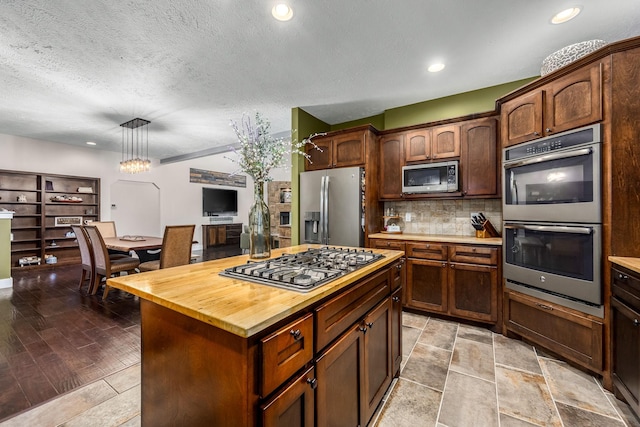 kitchen with wood counters, a center island, appliances with stainless steel finishes, pendant lighting, and backsplash